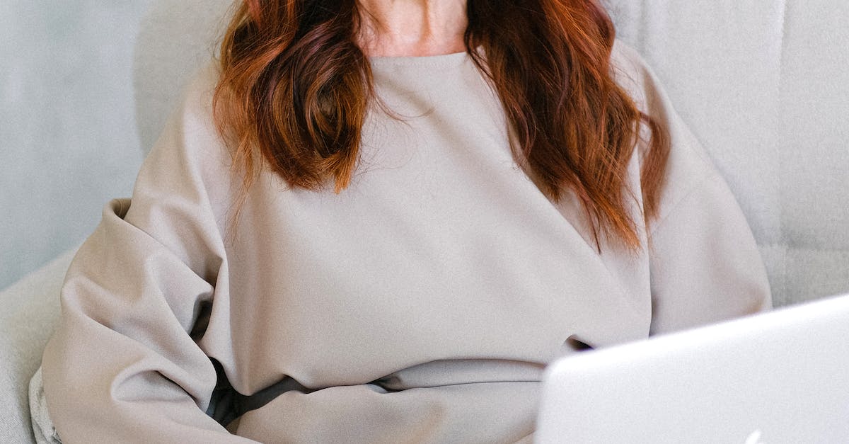Cheerful senior woman entrepreneur with long red hair in dress sitting on comfortable sofa and browsing laptop at home