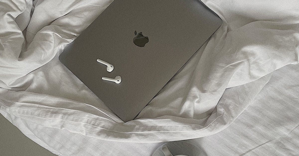 A Laptop and Airpods on the Bed Near the Cup of Coffee