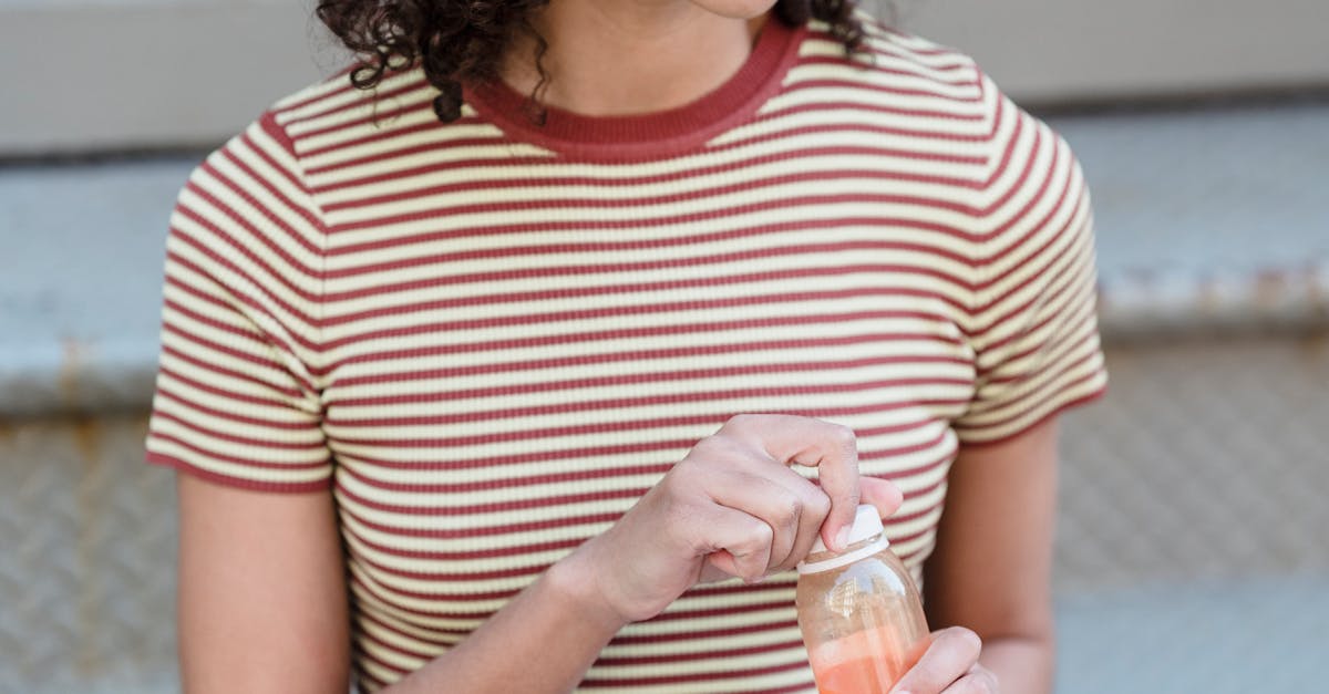 Happy young ethnic female student with curly hair in trendy outfit smiling and looking away while drinking fresh juice sitting on stairs on street with modern laptop on knees