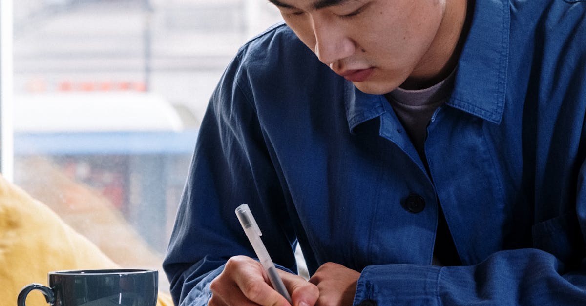 Man in Blue Dress Shirt Writing on White Paper