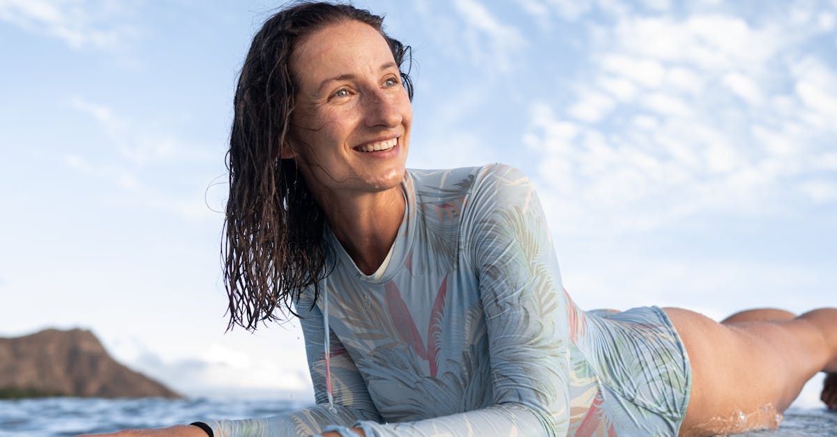 Happy young female traveler with wet hair lying on surfboard and looking away after training in wavy ocean on sunny day