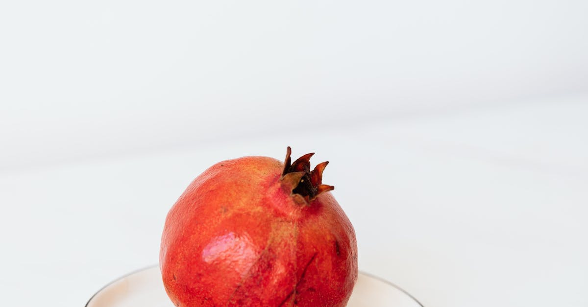 Whole ripe pomegranate placed on white metal plate on white table surface against gray background