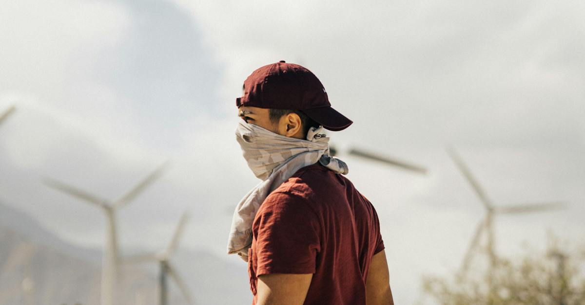 Unrecognizable man with scarf on face walking in sandy terrain terrain near windmills